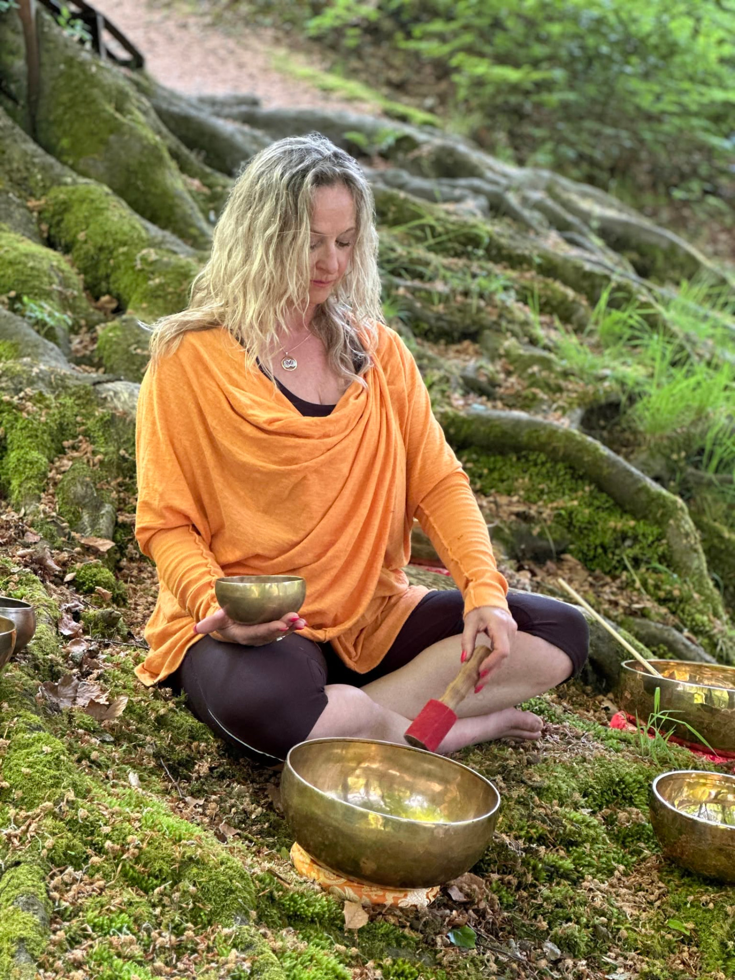 Jo from Sound Body Balance playing Himalayan singing bowls outdoors among mossy tree roots